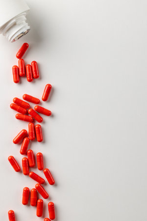 Vertical composition of white pill box spilling red pills on white background with copy space. Medicine, medical services, healthcare and health awareness concept.の写真素材