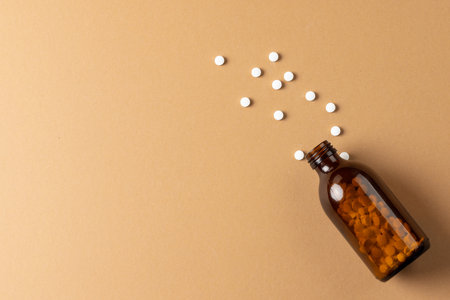 Composition of brown glass pill bottle spilling white pills on brown background with copy space. Medicine, medical services, healthcare and health awareness concept.の写真素材