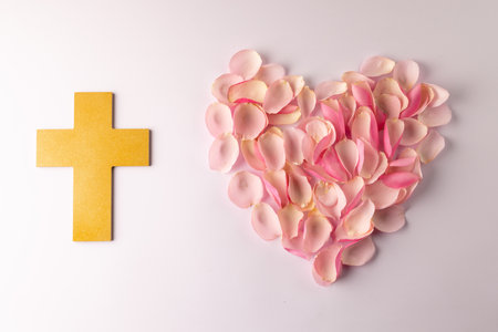 Overhead of yellow christian cross and heart shape of pink rose petals on white background. Love, faith and religion concept.の写真素材
