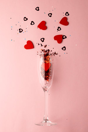 Vertical of champagne glass spilling red heart shapes on pale pink background with copy space. Valentine&#39;s day, love, romance and celebration concept.の写真素材