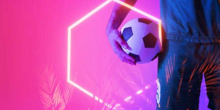 Midsection of caucasian male player holding soccer ball over illuminated hexagon and plants. Pink, copy space, digital composite, sport, soccer, competition, neon, glowing and abstract concept.の写真素材