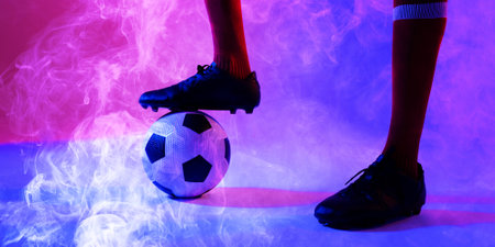 Low section of african american male player with leg on ball amidst smoky background. Copy space, digital composite, sport, soccer, competition, shoe, socks and abstract concept.の写真素材