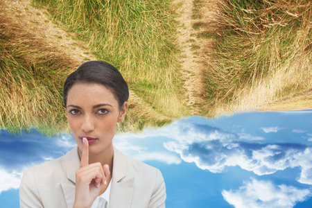 Biracial businesswoman with finger on lips against upside down grass and blue sky with copy space. Business conceptの写真素材