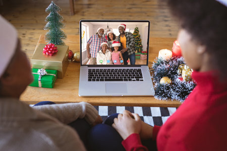 African american couple having christmas video call with african american family. Communication technology and christmas, digital composite image.の写真素材