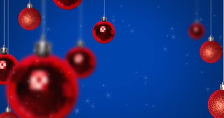 Image of snow falling over christmas bauble decorations on blue background. christmas, winter, tradition and celebration concept digitally generated image.の写真素材