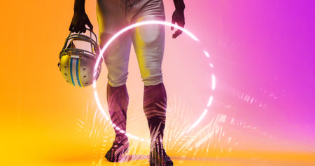 Low section of american football player holding helmet walking by illuminated circle and plants....