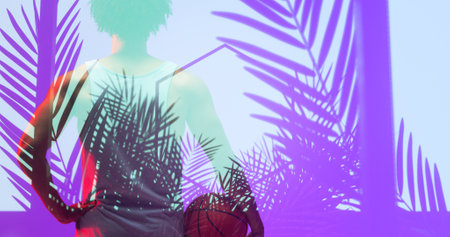 Rear view of biracial basketball player with ball standing over illuminated hexagon and plants. Composite, sport, competition, illustration, glowing, nature, shape and abstract concept.の写真素材