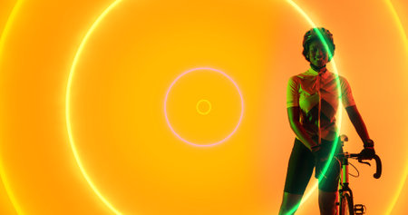 Biracial smiling female athlete with bike standing by illuminated circles on yellow background. Copy space, composite, sport, cycling, racing, competition, shape and abstract concept.の写真素材