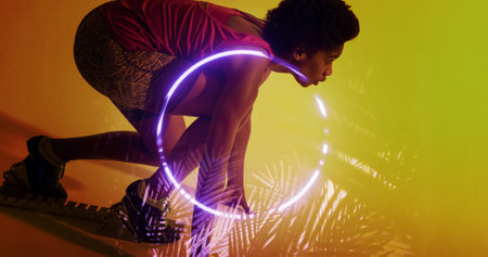 Side view of biracial female athlete bending at starting position by illuminated plants and circle....