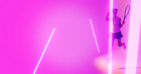 Full length of cheerful biracial female tennis player with racket running by illuminated lights. Copy space, composite, sport, competition, playing, match, winning, line, glowing and abstract.の写真素材