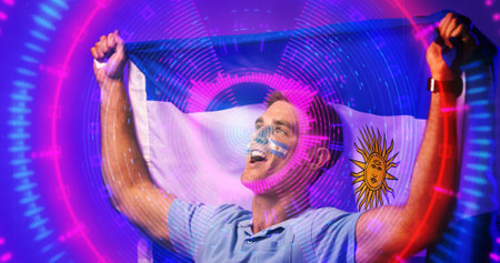 Cheerful caucasian soccer player with argentina flag screaming over illuminated circles. Composite, sport, competition, patriotism, shape, achievement, face paint, arms raised and abstract concept.の写真素材