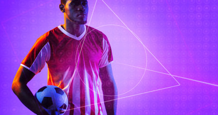 African american soccer player holding ball by geometric neon design over purple background. Computer graphic, copy space, digital composite, soccer, design, athlete, competitive sport.の写真素材