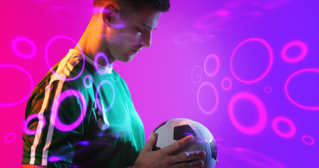 Composite of young caucasian player holding soccer ball with neon pattern in background, copy space. Computer graphic, soccer, design, athlete, competitive sport.の写真素材
