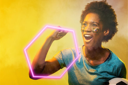 Hexagon neon over african american female fan with flag cheering during soccer match, copy space....
