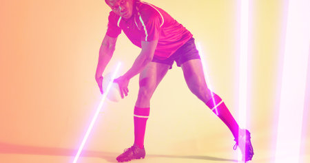 Low section of african american rugby player holding ball by glowing lights over beige background....
