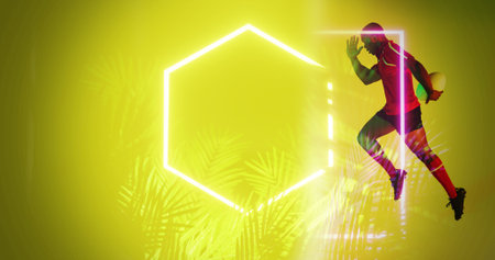 African american rugby player with ball running by plants and hexagon on yellow background. Illuminated, copy space, composite, sport, competition, shape, nature, playing, match and abstract concept.の写真素材