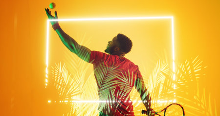 Rear view of african american male tennis player serving ball by illuminated plants and rectangle....
