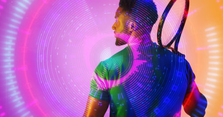 Illuminated circular patterns over rear view of african american tennis player holding racket. Composite, sport, competition, playing, match, shape, glowing and abstract concept.の写真素材