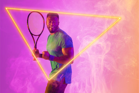 Happy african american male tennis player with racket shaking fists by illuminated triangle. Copy space, composite, sport, competition, shape, playing, winner, match and abstract concept.の写真素材