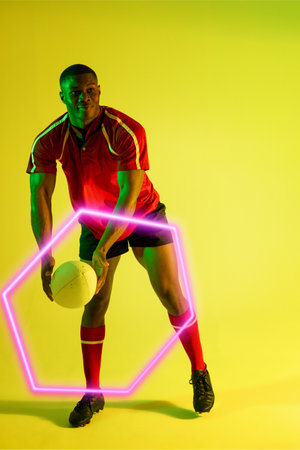 Smiling african american male player throwing rugby ball by illuminated hexagon on green background. Copy space, composite, sport, competition, shape, playing, match and abstract concept.の写真素材