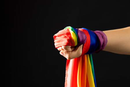 Hand holding rainbow coloured flag with copy space on black background. Pride month, equality, lgbt...