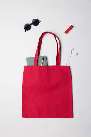 High angle view of red canvas bag with notebook, sunglasses, earphones and lighter, copy space. Bags and fashion concept.の写真素材
