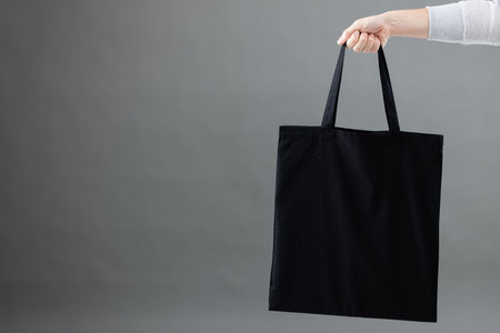 Hand of caucasian woman holding black canvas bag with copy space on grey background. Bags and fashion concept.の写真素材