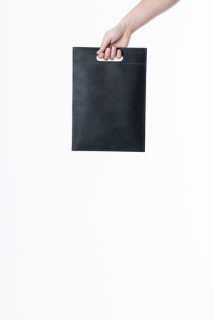Hand of caucasian woman holding black bag with copy space on white background. Bags and fashion...
