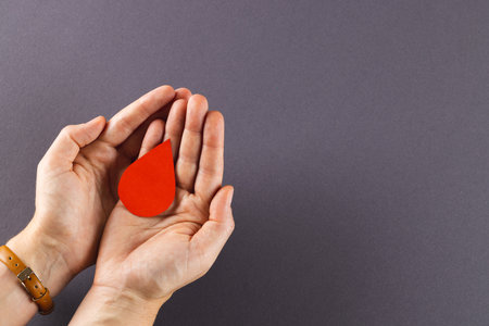 Hands of caucasian woman cupping blood drop, on grey background with copy space. Blood donation, medicine and healthcare.の写真素材