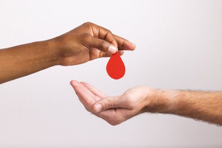 Hands of biracial man giving blood drop to caucasian man, on white background. Blood donation, medicine and healthcare.の写真素材