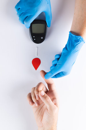 Hands of gloved doctor with glucometer taking blood sugar reading from caucasian woman. Blood sugar, diabetes and health awareness.の写真素材