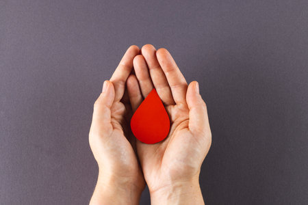 Hands of caucasian woman cupping blood drop, on grey background with copy space. Blood donation, medicine and healthcare.の写真素材