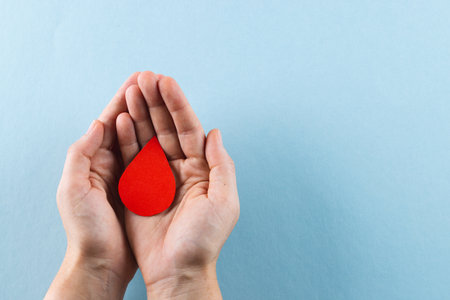 Hands of caucasian woman cupping blood drop, on blue background with copy space. Blood donation, medicine and healthcare.の写真素材