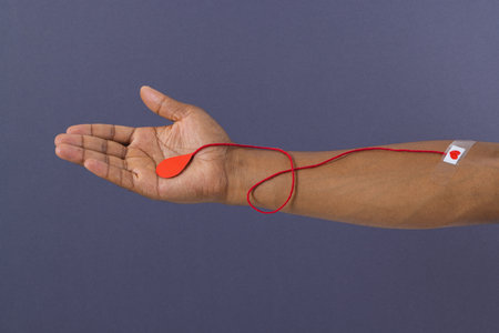 Arm of biracial man with heart sticking plaster and red string with blood drop, on grey background....