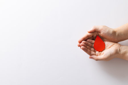 Hands of caucasian woman cupping blood drop, on white background with copy space. Blood donation, medicine and healthcare.の写真素材