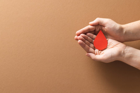 Hands of caucasian woman cupping blood drop, on brown background with copy space. Blood donation, medicine and healthcare.の写真素材