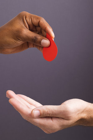 Hands of biracial man giving blood drop to caucasian man, on grey background with copy space. Blood donation, medicine and healthcare.の写真素材