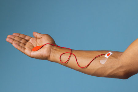 Arm of biracial man with heart sticking plaster and red string with blood drop, on blue background. Blood donation, medicine and healthcare.の写真素材