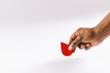 Hand of biracial man holding blood drop above slot, on white background with copy space. Blood donation, blood bank, medicine and healthcare.の写真素材
