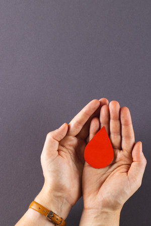 Hands of caucasian woman cupping blood drop, on grey background with copy space. Blood donation, medicine and healthcare.の写真素材