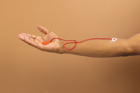 Arm of biracial man with heart sticking plaster and red string with blood drop, on brown background. Blood donation, medicine and healthcare.の写真素材
