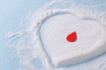 Blood drop over sugar in heart shape on blue background. Diet, blood sugar, diabetes and heart health awareness.の写真素材