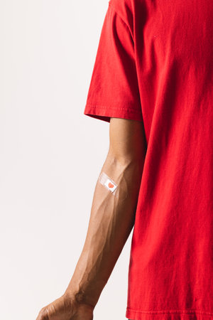 Midsection of biracial man with heart sticking plaster on arm, on white background. Blood donation,...