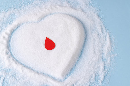 Blood drop over sugar in heart shape on blue background. Diet, blood sugar, diabetes and heart health awareness.の写真素材