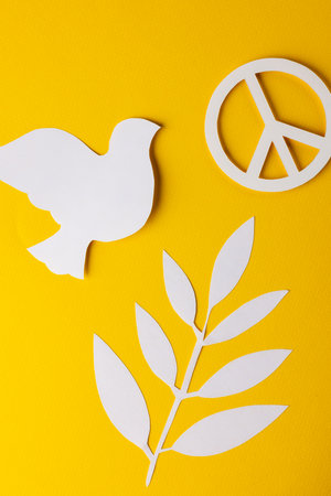 High angle view of white peace sign, white dove and leaf with copy space on yellow background. Peace and anti war movement concept.の写真素材