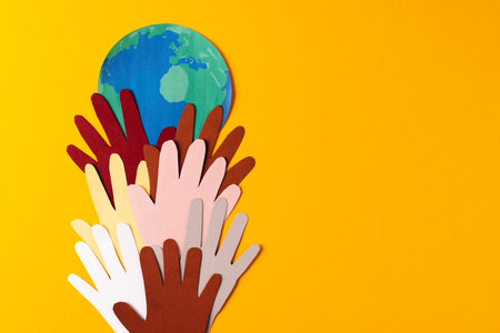Paper cut out of multi coloured hands and globe with copy space on yellow background. Humanitarian aid, people, help and human concept.の写真素材