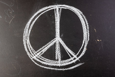 Close up of white chalk peace sign on black chalkboard background. Peace and anti war movement concept.の写真素材