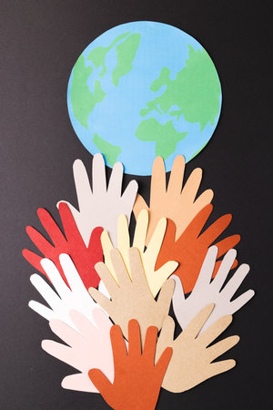 Paper cut out of multi coloured hands and globe with copy space on black background. Humanitarian...