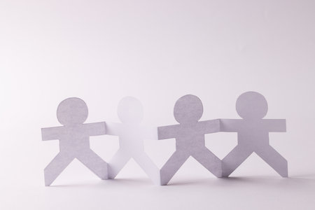 Close up of four paper cut out people figures holding hands with copy space on white background. Humanitarian, people, help and human concept.の写真素材