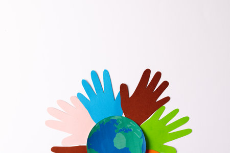 Paper cut out of multi coloured hands and globe with copy space on white background. Humanitarian aid, people, help and human concept.の写真素材